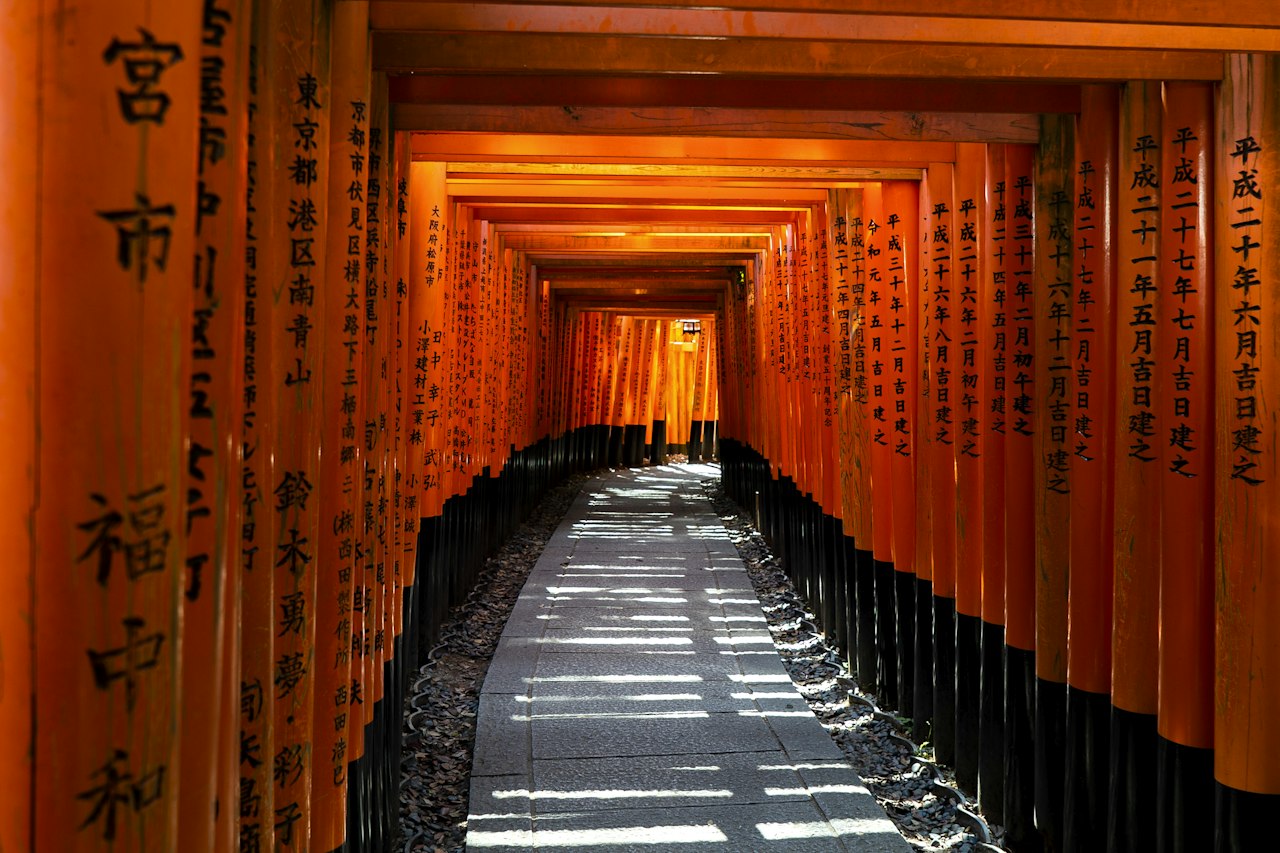 A stone path through a tunnel of orange torii gates in Kyoto, Japan