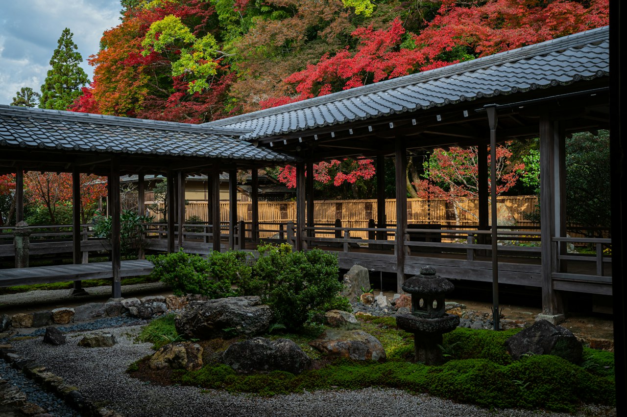 A wooden covered walkway in a Japanese garden with vibrant autumn foliage