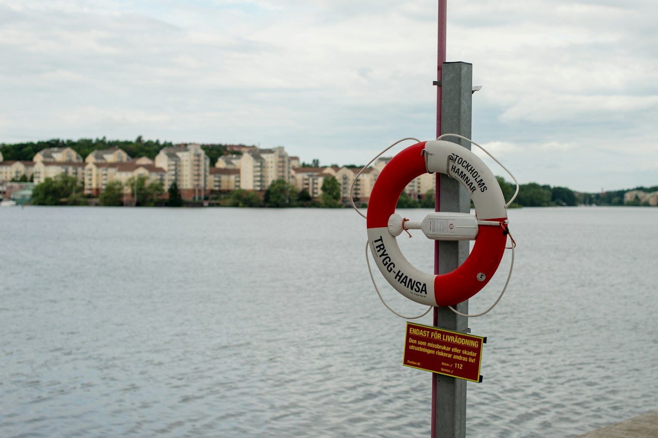 Life preserver hangs on pole with buildings across water